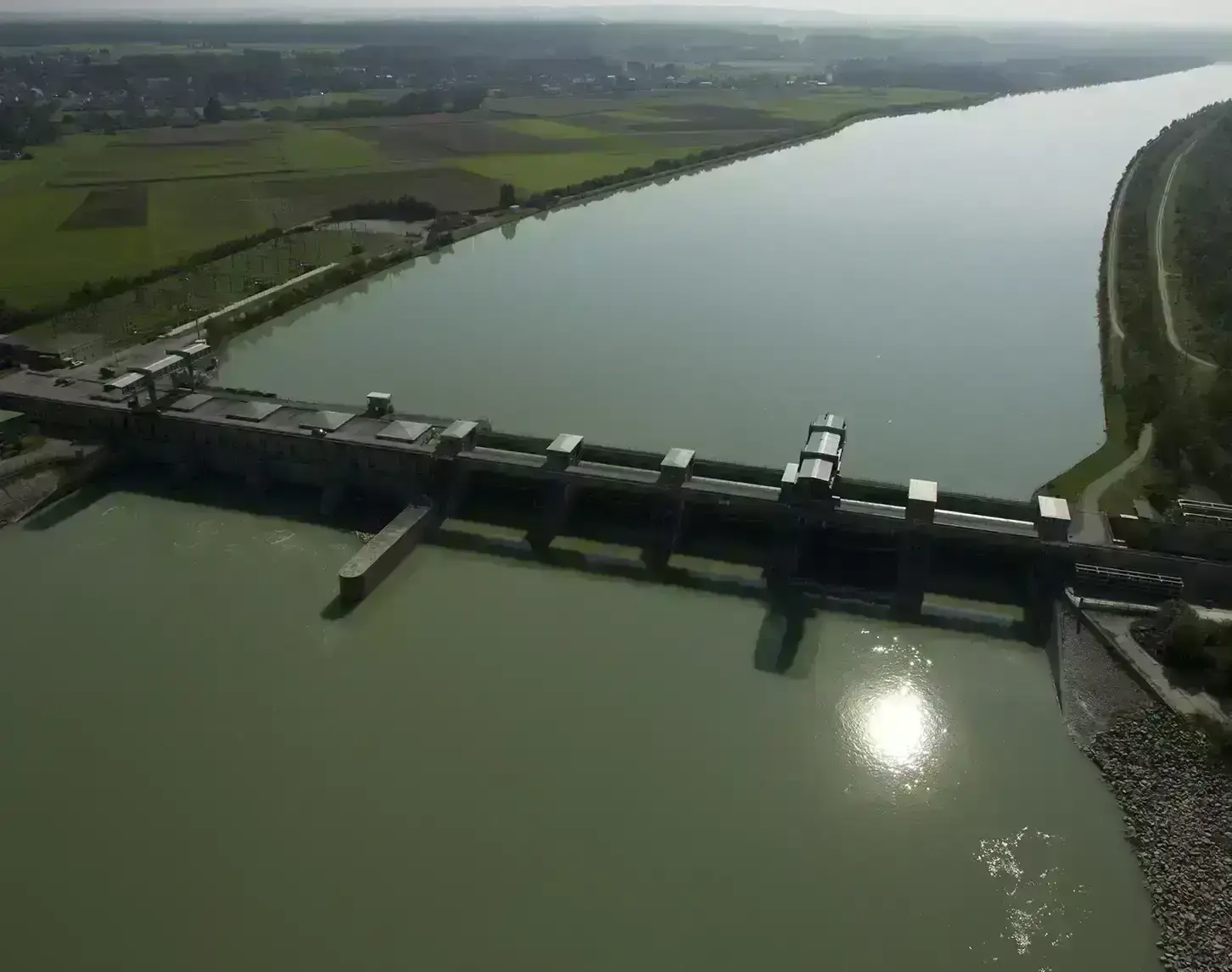 Aerial view of a run-of-river power plant on a river, surrounded by farmland on a sunny day.