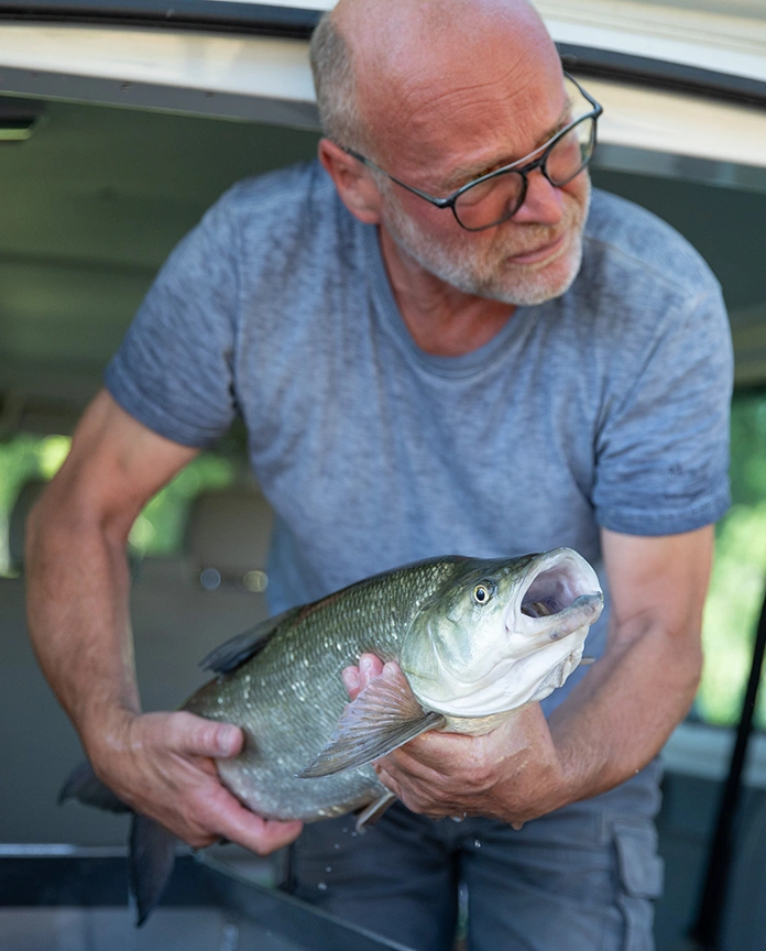 Person in blauem T-Shirt hält stolz einen großen Fisch in den Händen.